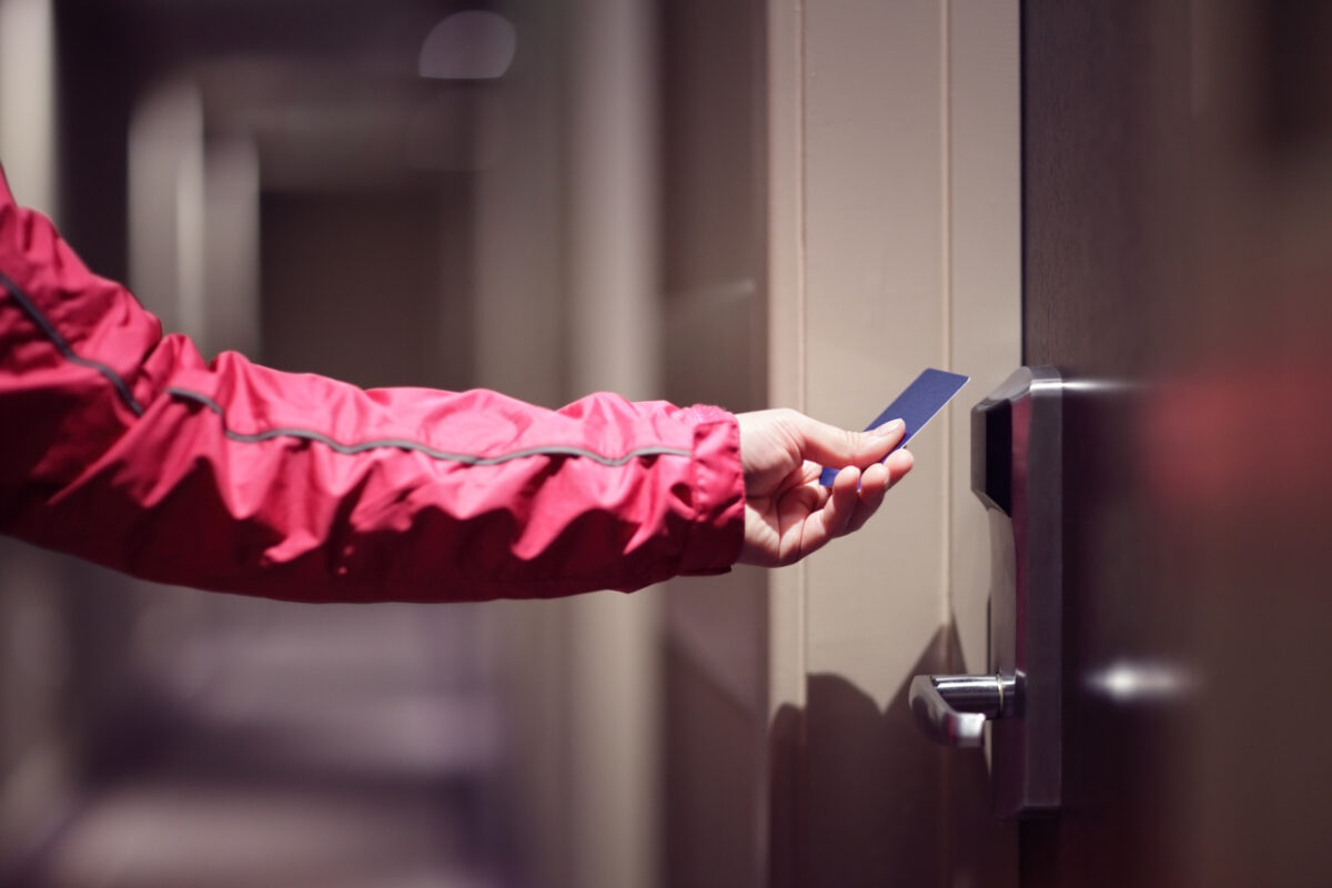 A hand is opening a hotel room door by scanning their key card