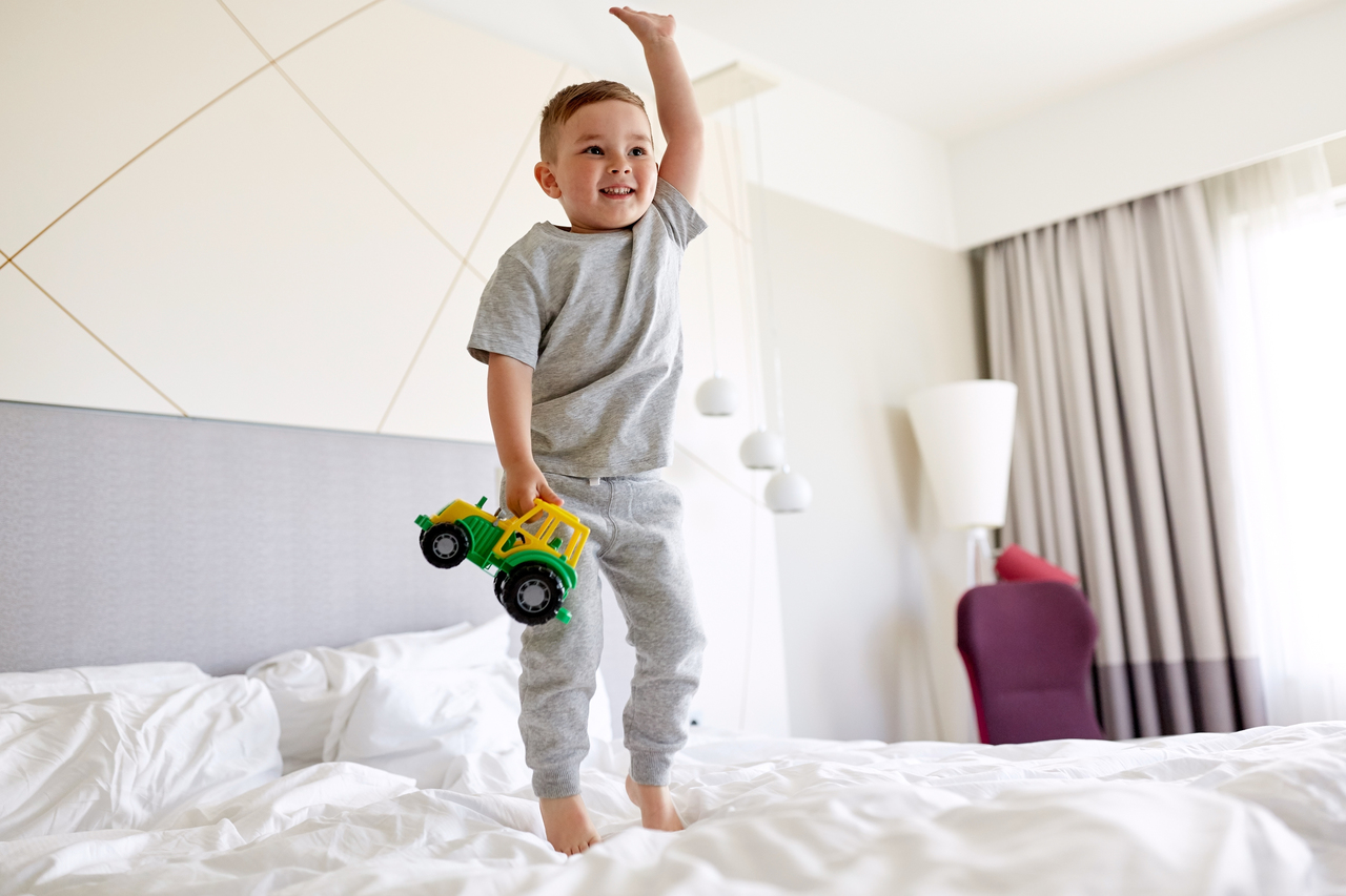 Little boy happily jumping on a hotel room bed
