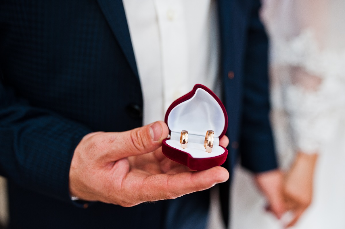 wedding rings at hand of groom on heart shaped box