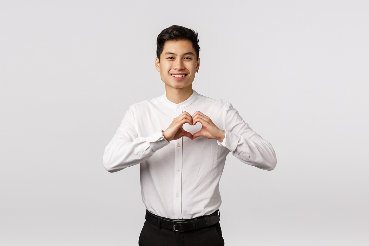 Lovely young asian boyfriend in formal shirt, pants, showing heart sign express love, affection or admiration, smiling camera, invite girlfriend go prom together, standing white background