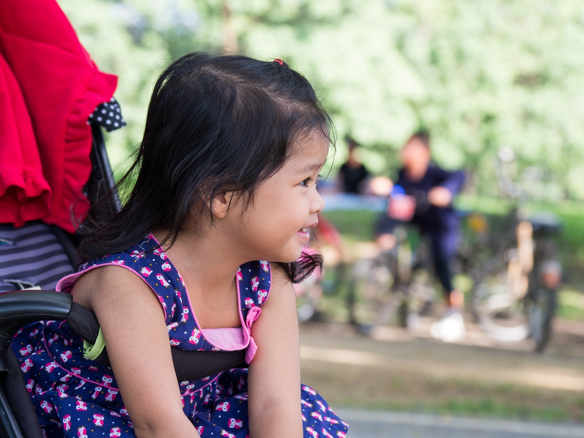 Little asian girl sitting in a stroller at public park. She have be smile.