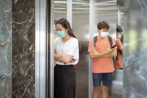Two people practicing social distancing in an elevator
